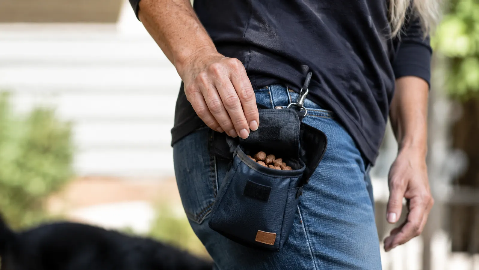 Close-up of a hand opening the magnetic closure on a dog treat pouch revealing small training treats inside